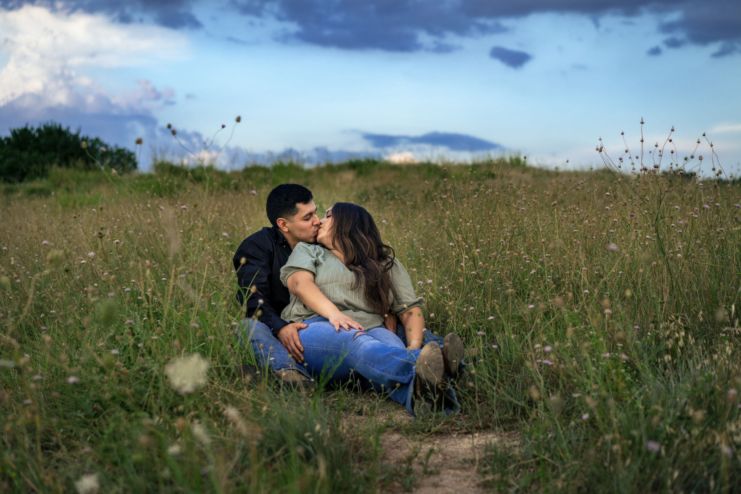 man and woman kiss while sitting together in a field of wildflowers