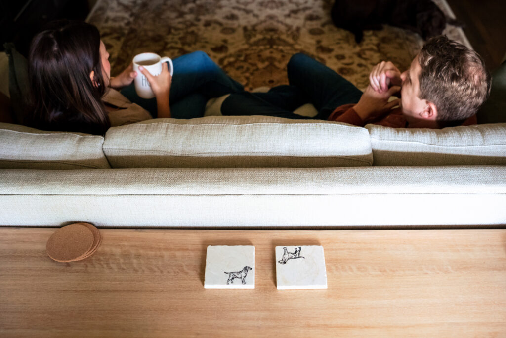 man and woman sit on a couch together while drinking coffee