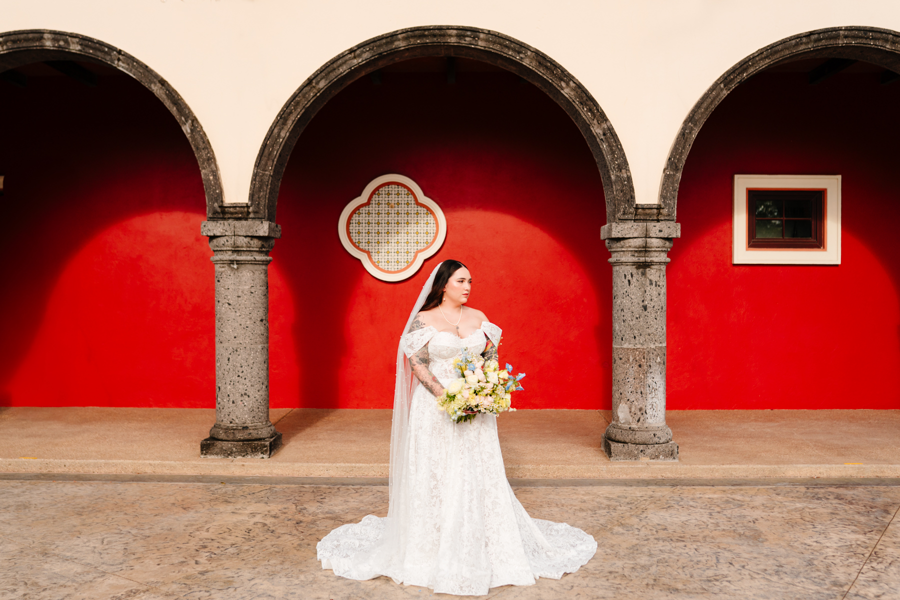 Bride standing under dramatic red archway at Mediterranean-inspired wedding venue in North Texas