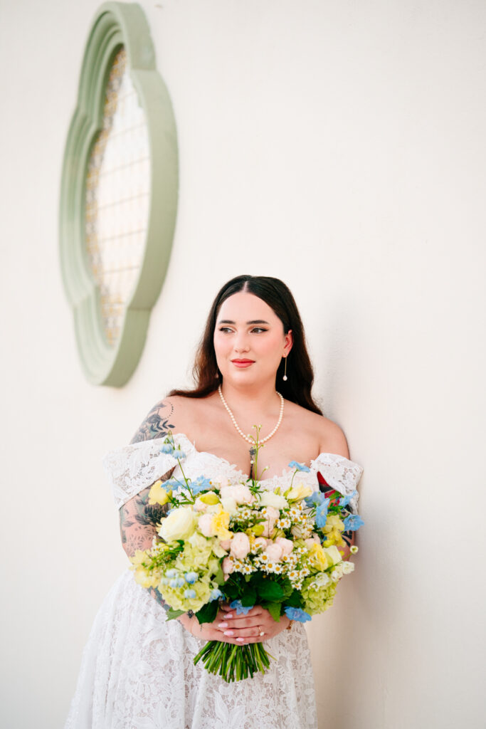 Bride holding bouquet against whitewashed wall with European-style window at Stoney Ridge Villa