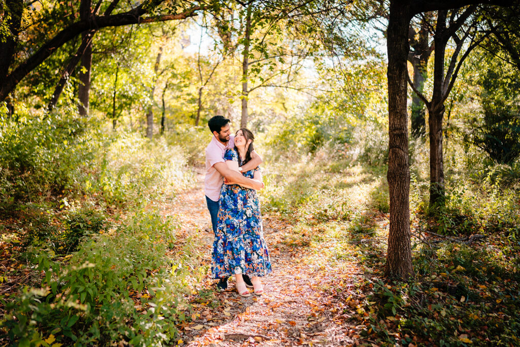 Couple embracing on a sunlit trail during their Dallas engagement session at Reverchon Park.