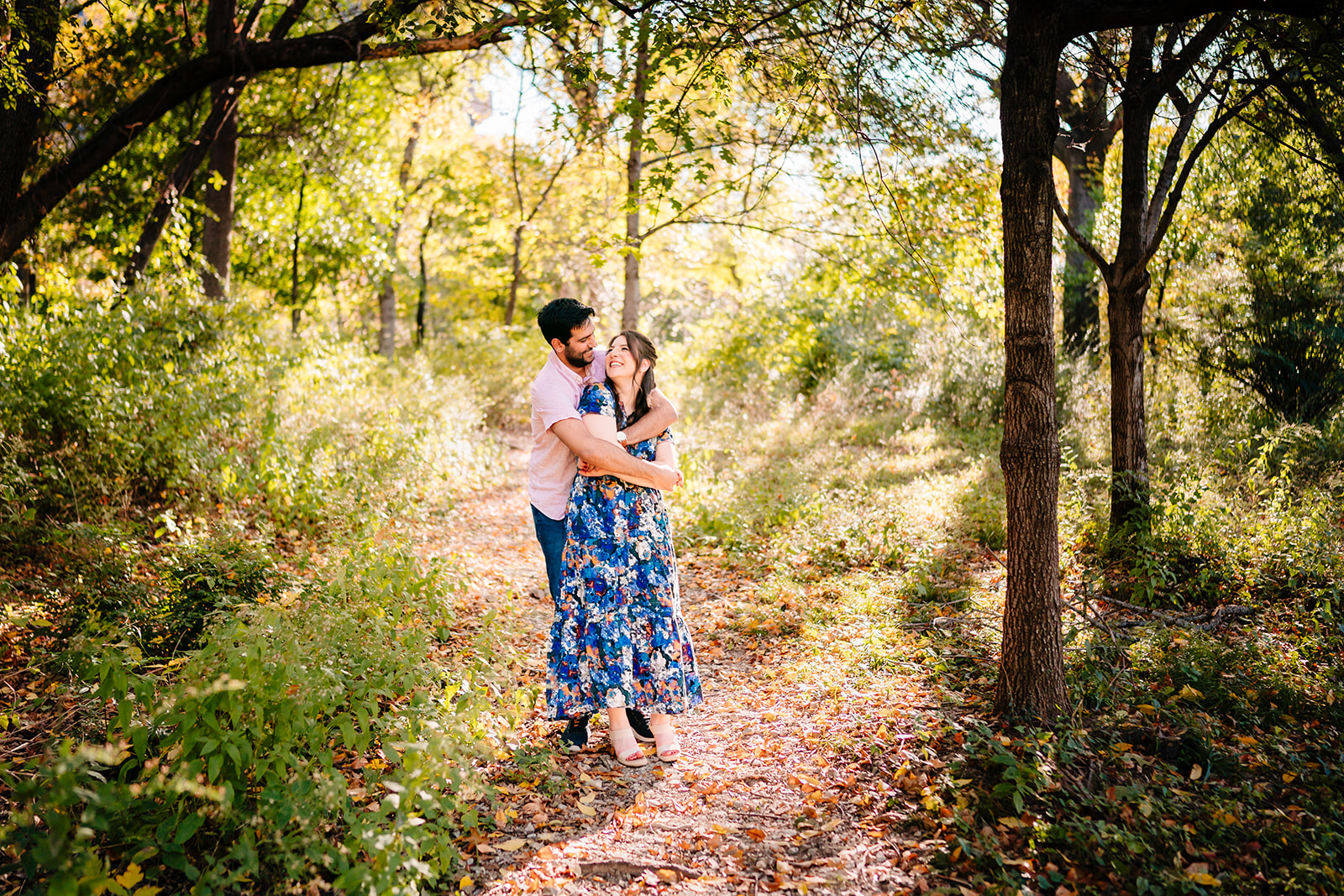 Couple embracing on a sunlit trail during their Dallas engagement session at Reverchon Park.