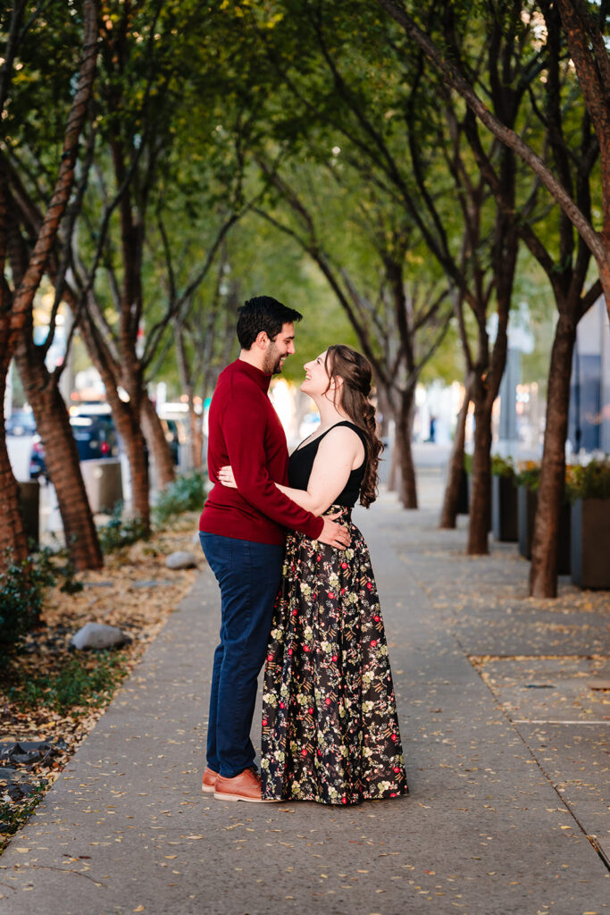 Couple embracing along tree covered pathway during their engagement session at the meyerson symphony center in downtown dallas