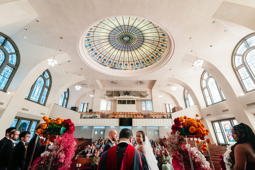 Bride and groom standing beneath stained glass windows at Tyler Street Church wedding