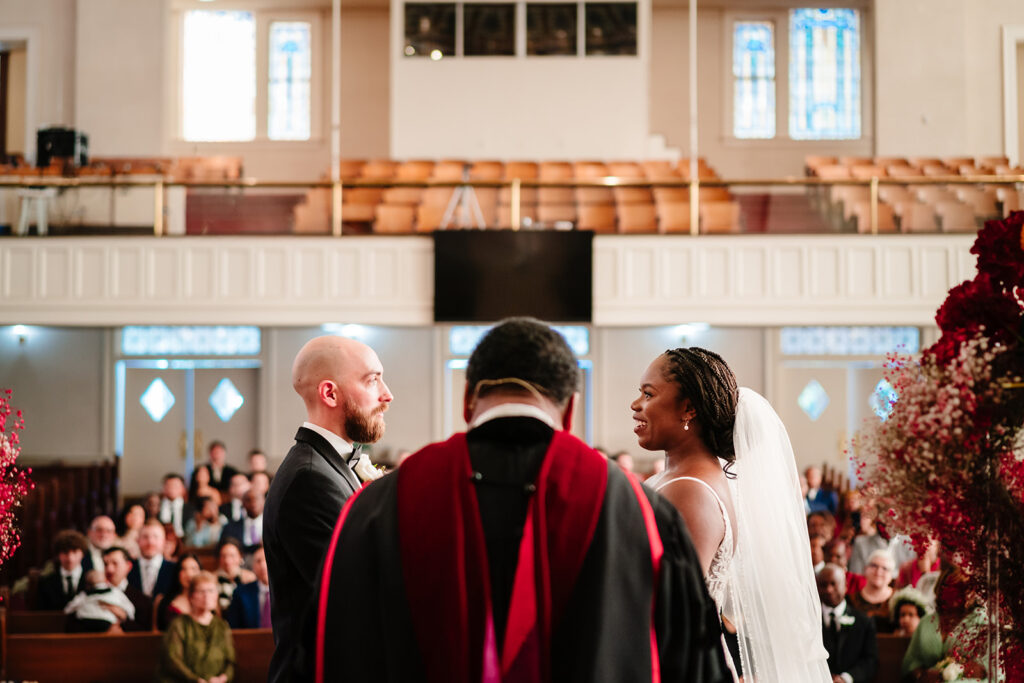 Ashley and Tom exchanging vows at Tyler Street Church in Dallas surrounded by stained glass windows
