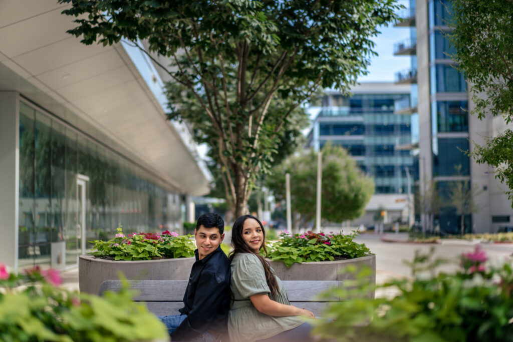 Man and woman sitting back to back with urban buildings behind them