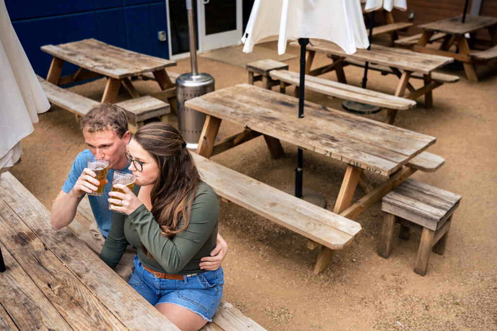 couple sits together at brewery picnic table while drinking beers