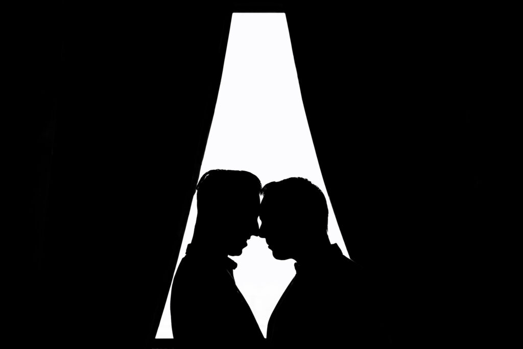 silhouette of men standing nose to nose near window