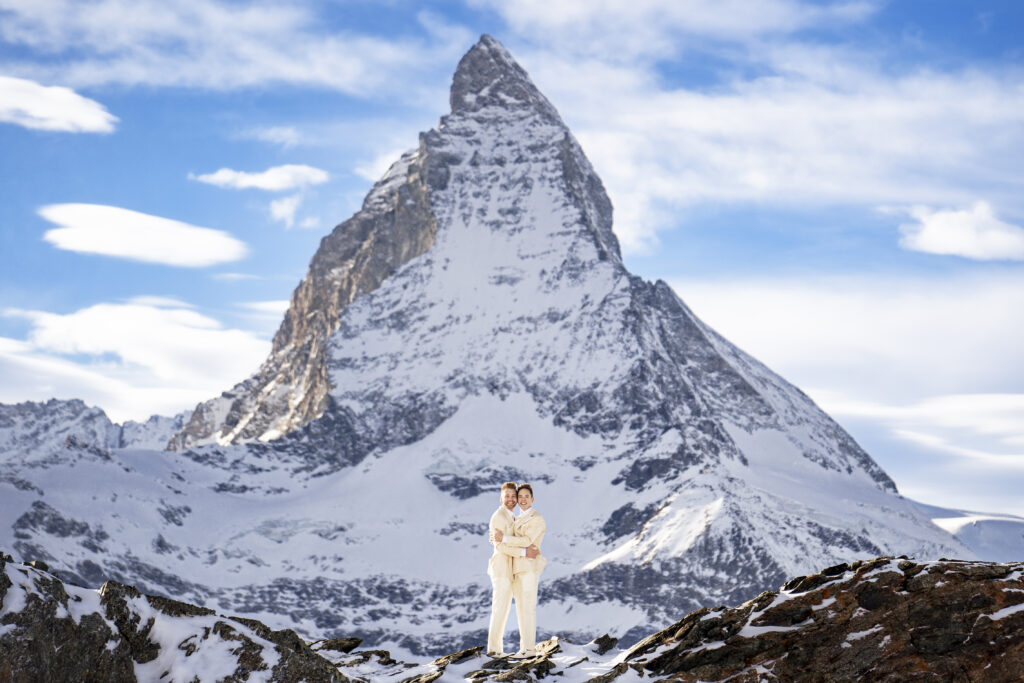 Matt & Brady standing in a snow-covered landscape with the Matterhorn in the background during their LGBTQ wedding portraits in Switzerland with documentary wedding photographers The MacMeekens